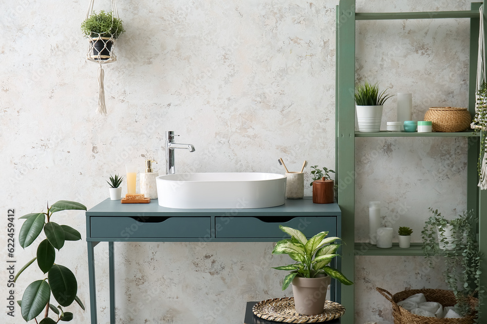 Interior of light bathroom with sink, shelving unit and houseplants