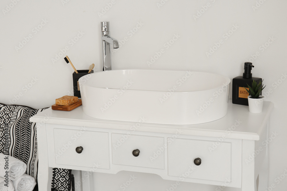 Sink with bath accessories on table near light wall in room