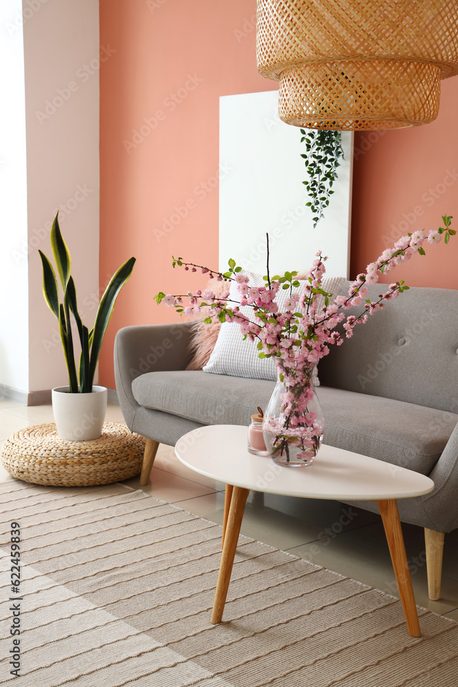 Vase with blooming sakura branches on coffee table in interior of living room