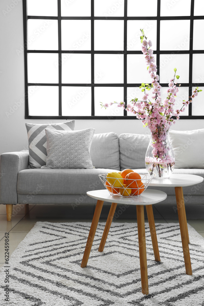 Interior of stylish living room with grey sofas and blooming sakura branches on coffee table