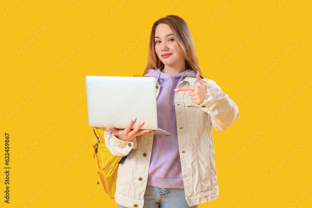 Female student pointing at laptop on yellow background