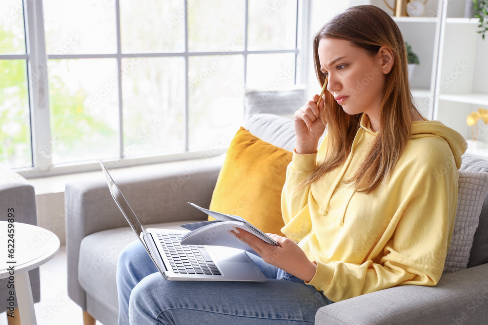 Thoughtful female student studying with notebook and laptop at home