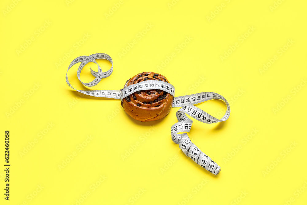 Tasty chocolate bun and measuring tape on yellow background. Diet concept