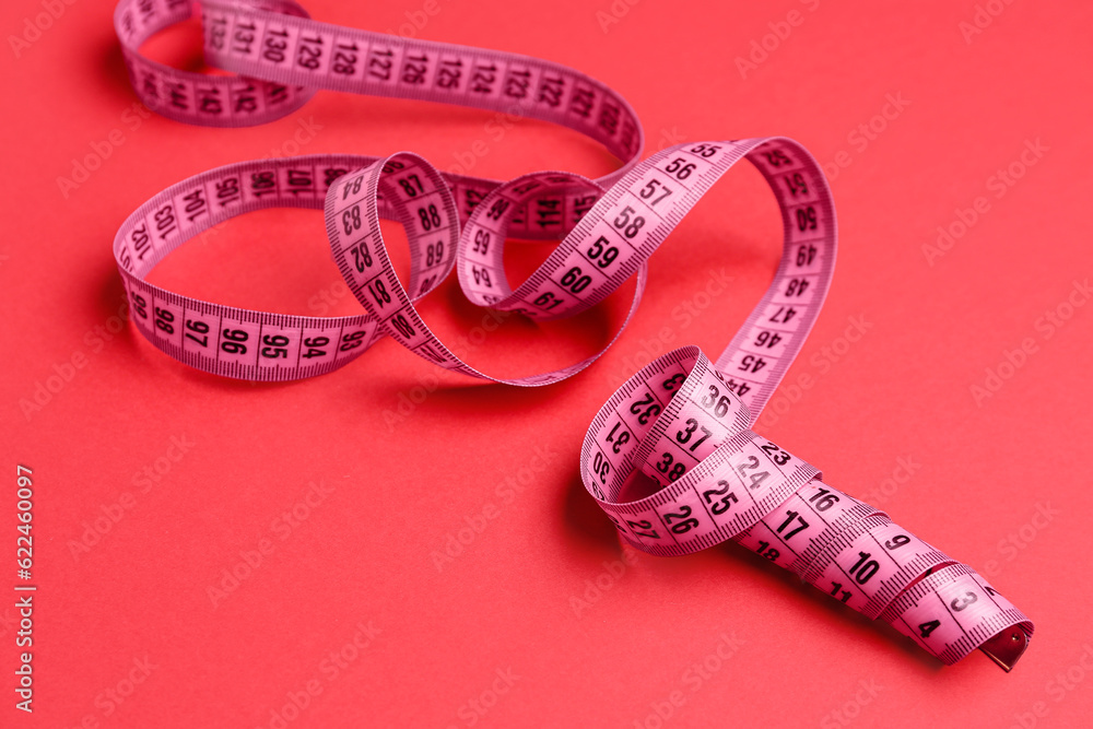 New measuring tape on red background, closeup