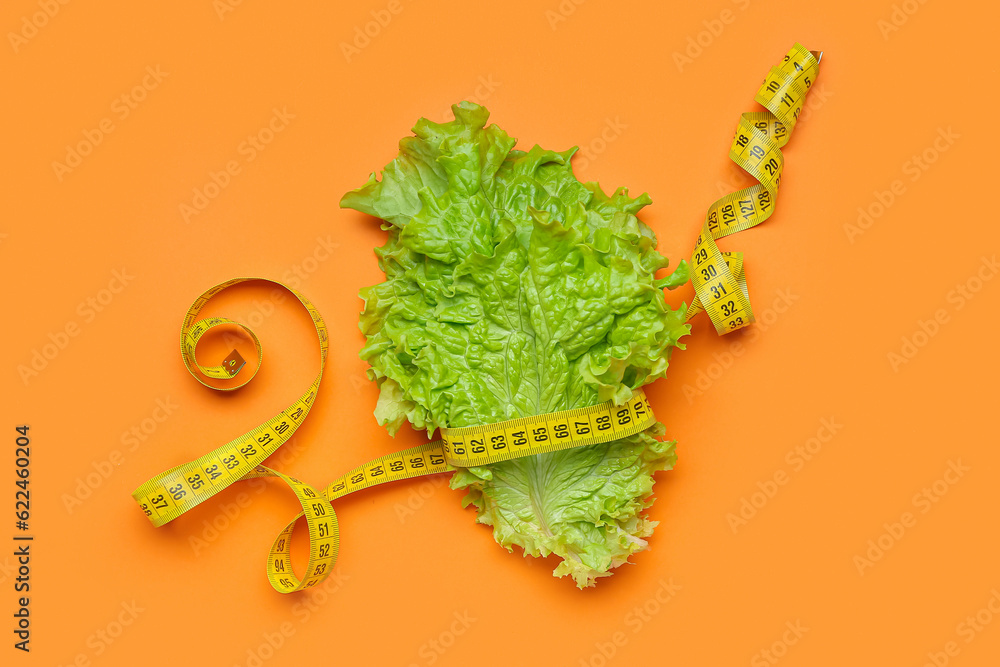 Lettuce and measuring tape on orange background. Diet concept