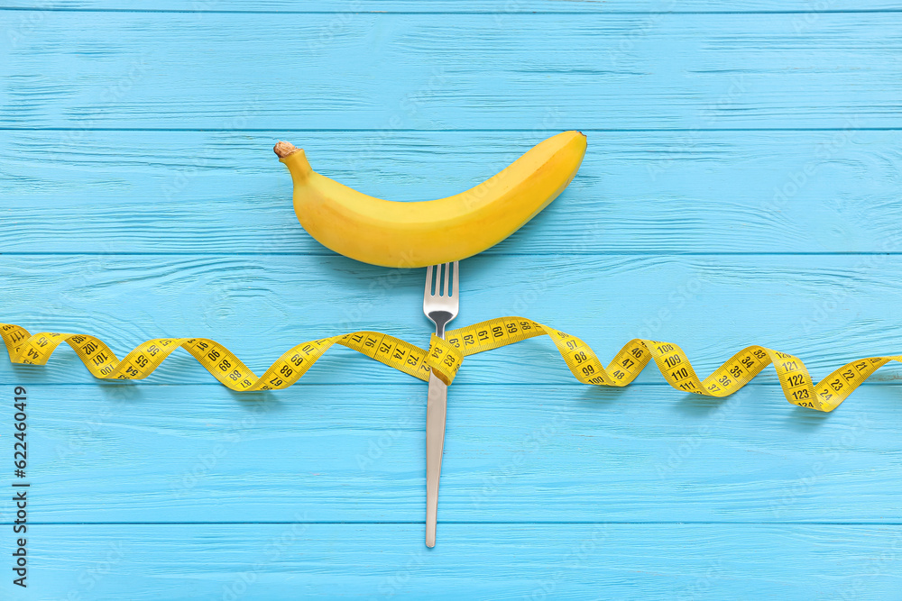 Composition with banana, fork and measuring tape on color wooden background. Diet concept