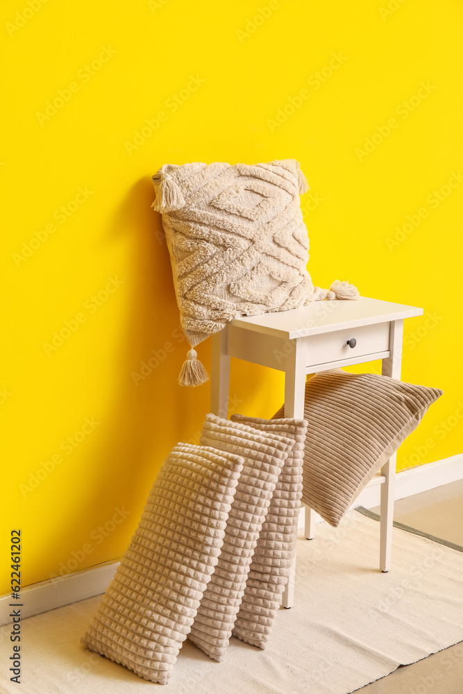 Table with stylish pillows near yellow wall in room