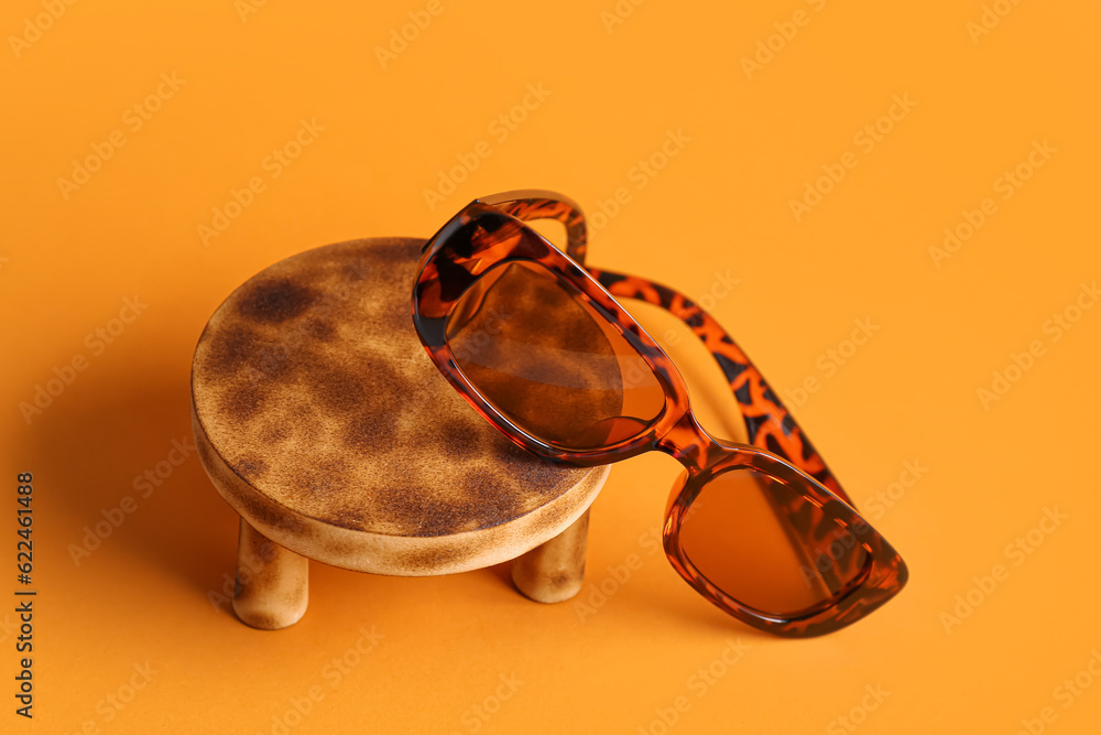 Stand with stylish eyeglasses on orange background, closeup