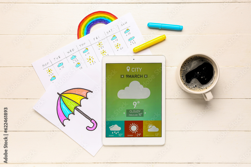 Tablet computer with weather forecast, drawn umbrella and cup of coffee on white wooden background