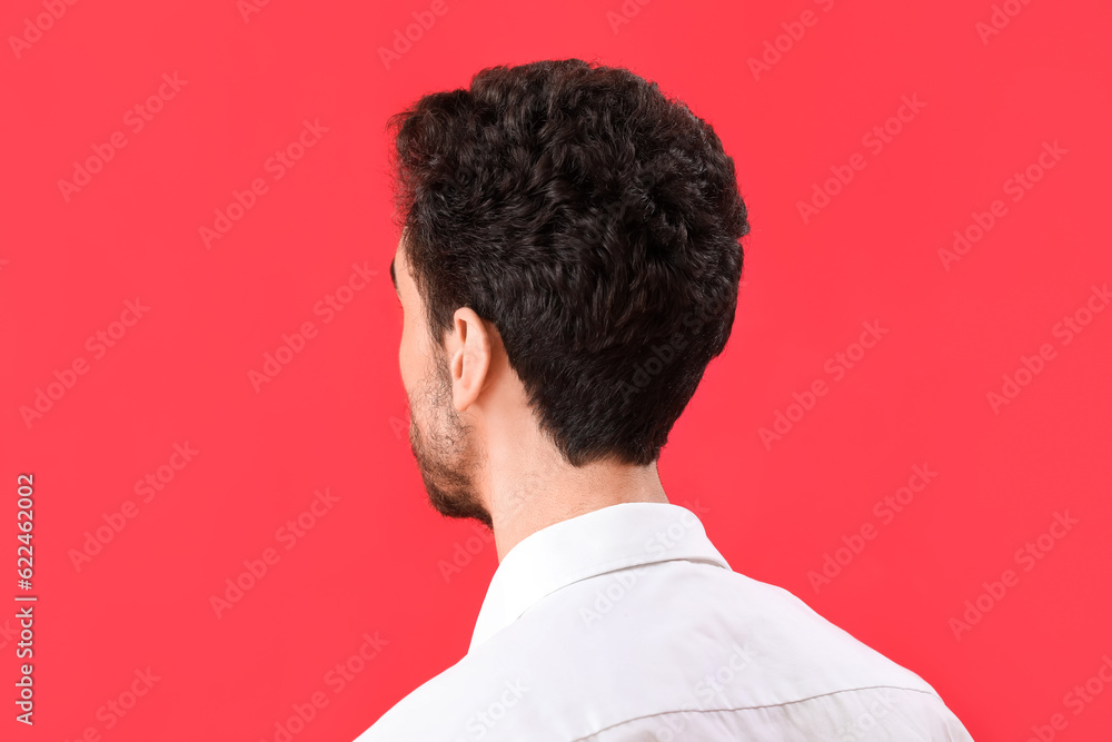 Young brunette man with stylish hairdo on red background, closeup