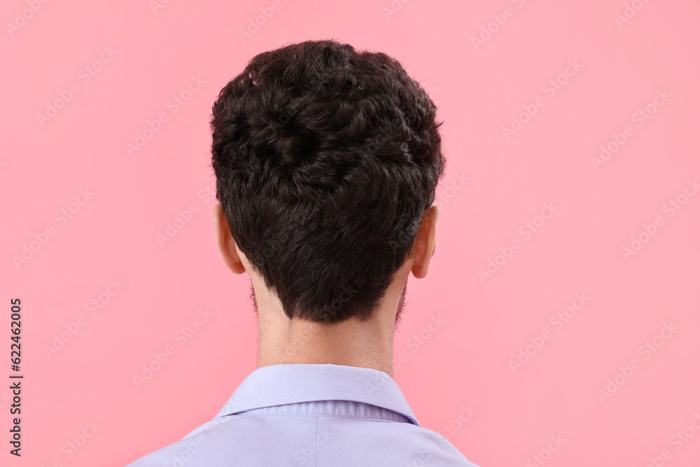 Young brunette man with stylish hairdo on pink background, back view