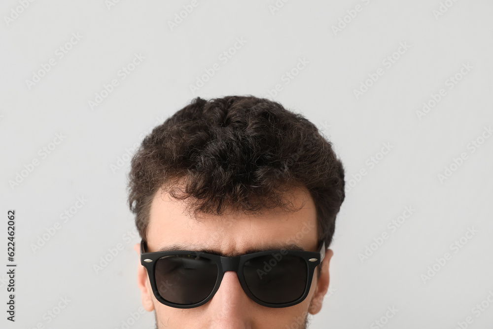 Young brunette man in sunglasses on light background, closeup