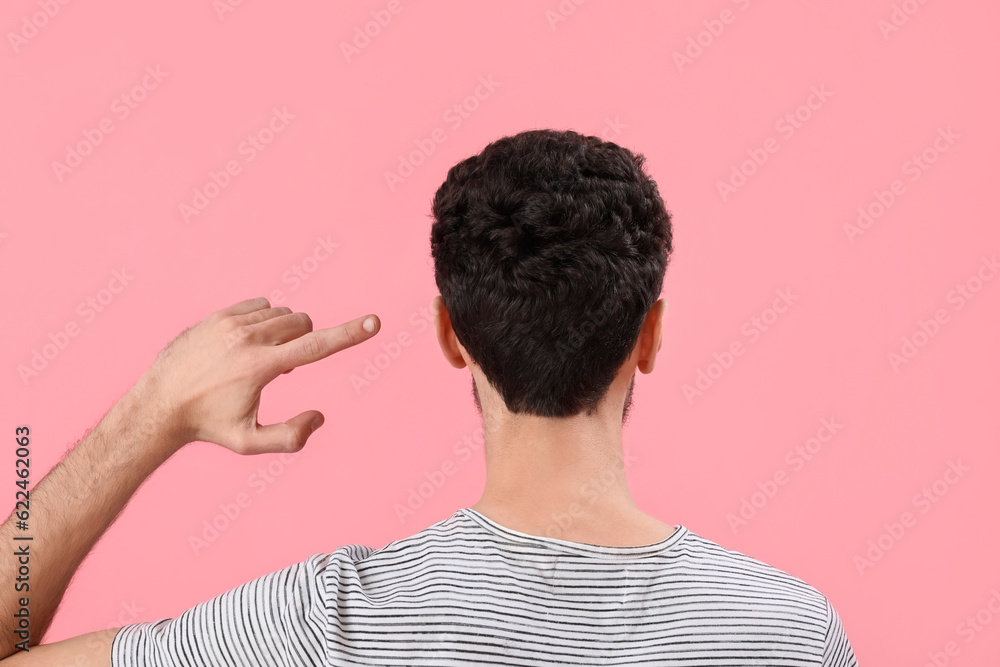 Young brunette man pointing at his hair on pink background, back view