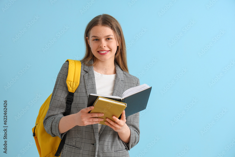 Happy female student with backpack and  different books on blue background