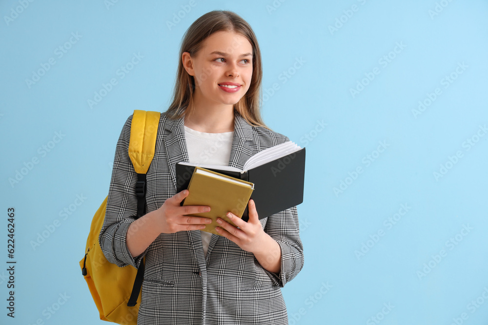 Happy female student with backpack and  different books on blue background