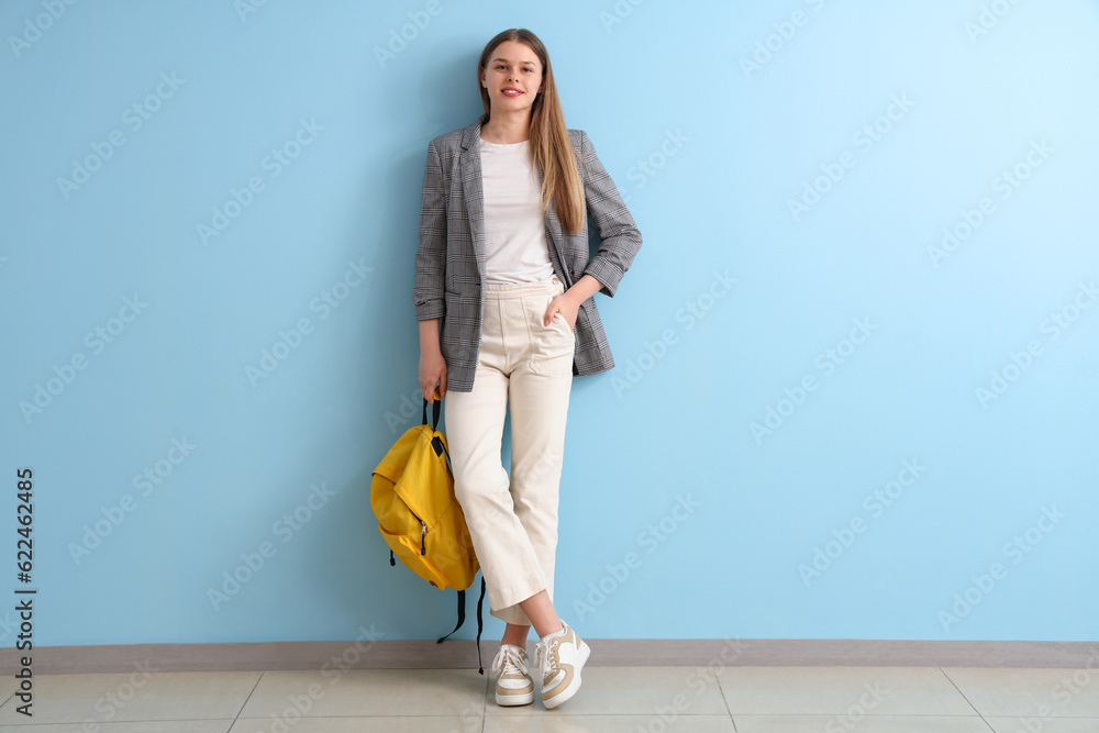 Female student with backpack near blue wall