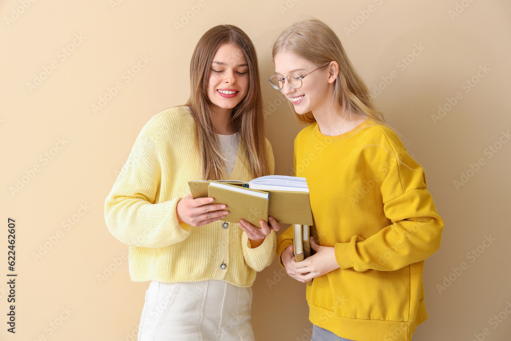 Happy female students reading book  on pale yellow background