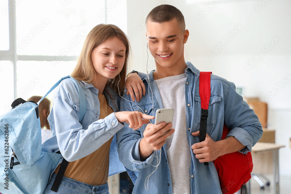 Happy students with backpacks using mobile phone in classroom