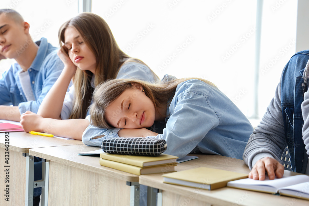 Tired sleepy classmates sitting at desks in classroom