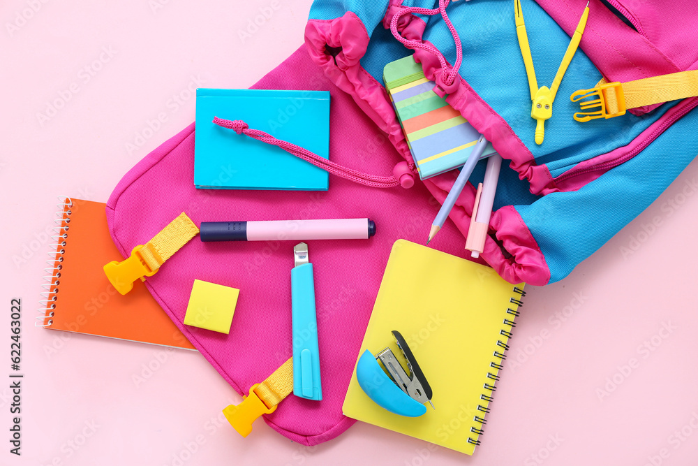 Color school backpack with notebooks and stationery on pink background