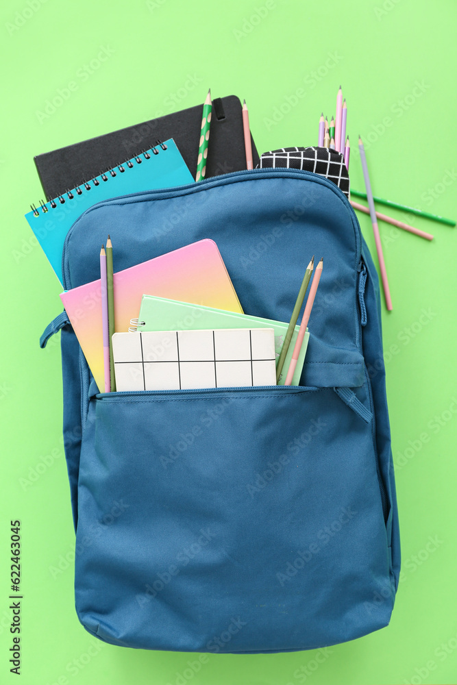 Blue school backpack with notebooks and pencils on green background