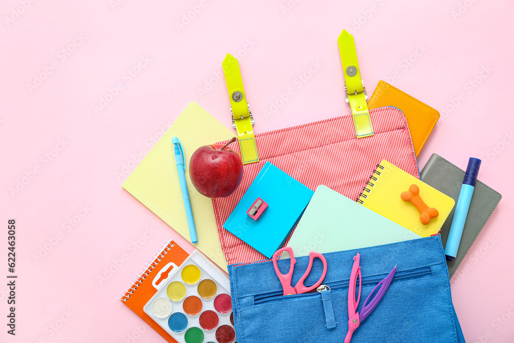 Blue school backpack with notebooks, watercolors and apple on pink background