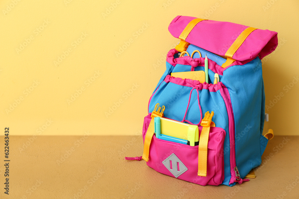 Color school backpack with notebooks, pens and marker on table near yellow wall