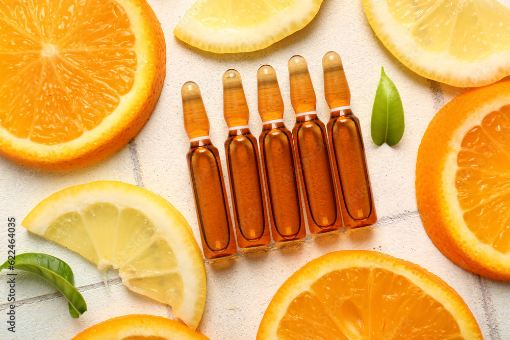 Ampoules with vitamin C and different citrus fruit slices on white tile background