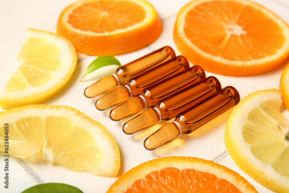 Ampoules with vitamin C and different citrus fruit slices on white tile background