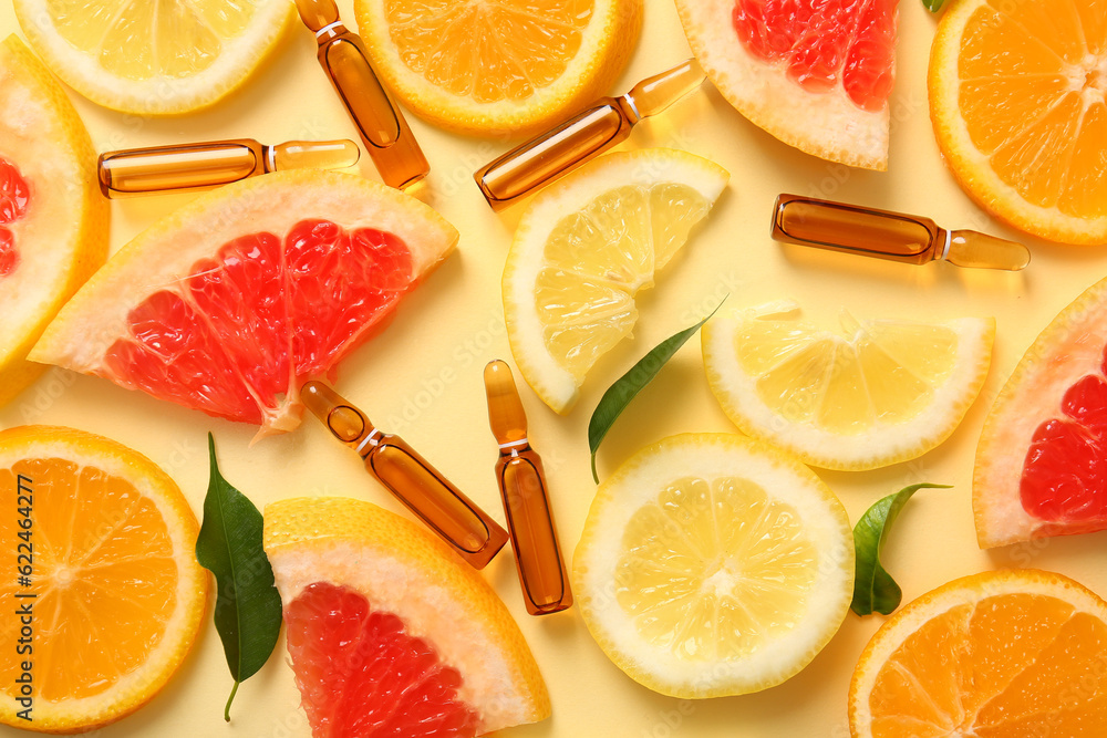 Ampoules with vitamin C and different citrus fruit slices on yellow background