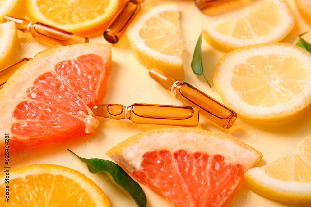 Ampoules with vitamin C and different citrus fruit slices on yellow background