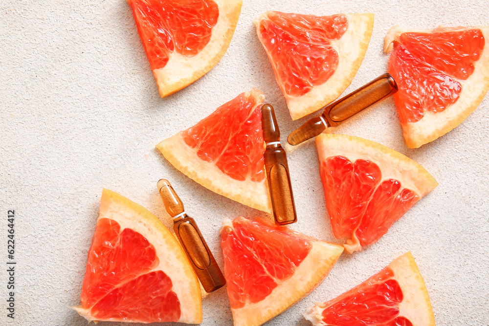 Ampoules with vitamin C and grapefruit pieces on light background