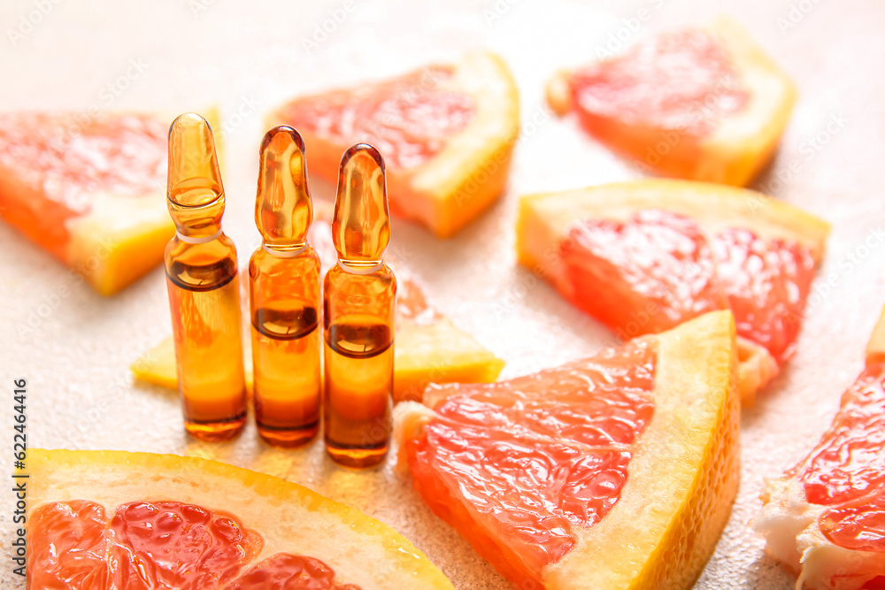 Ampoules with vitamin C and grapefruit pieces on light background, closeup