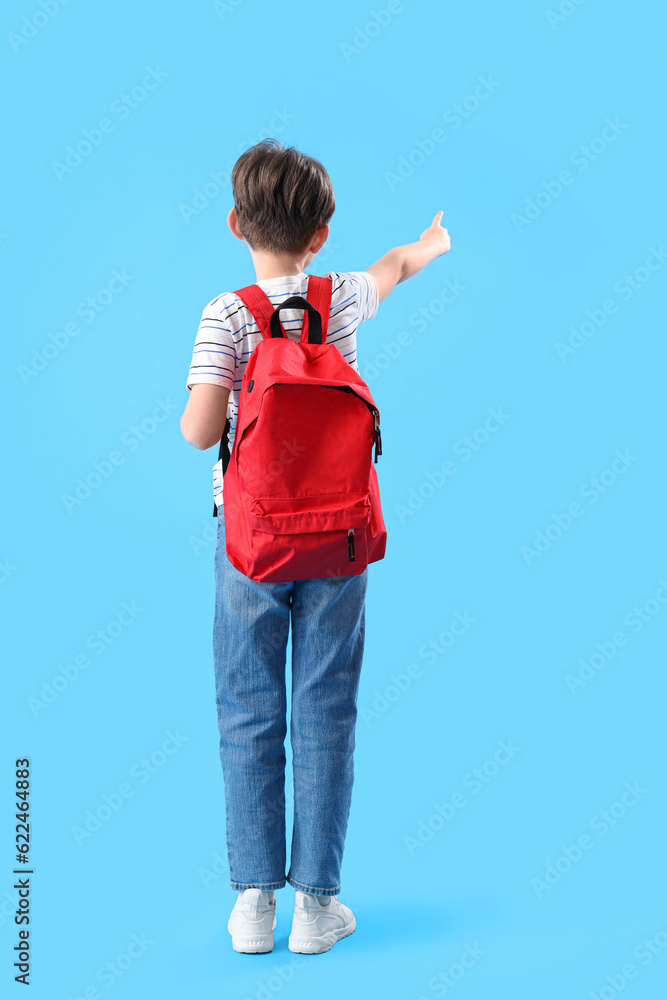 Little boy with schoolbag pointing at something on blue background, back view