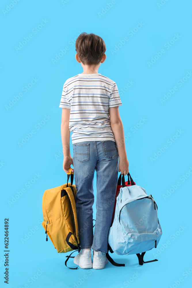 Little schoolboy with backpacks on blue background, back view