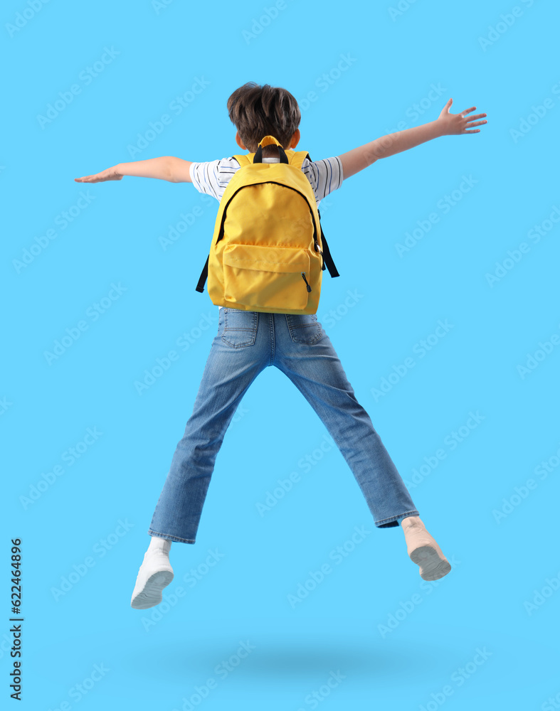 Jumping little boy with schoolbag on blue background, back view