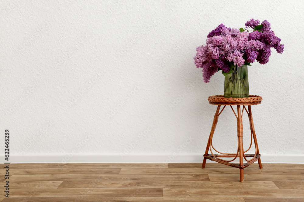 Vase with beautiful lilac flowers on table near light wall in room