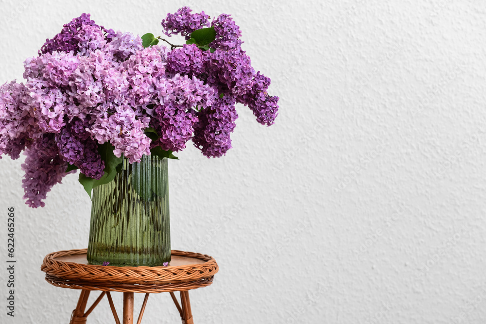 Vase with beautiful lilac flowers on table near white wall in room, closeup