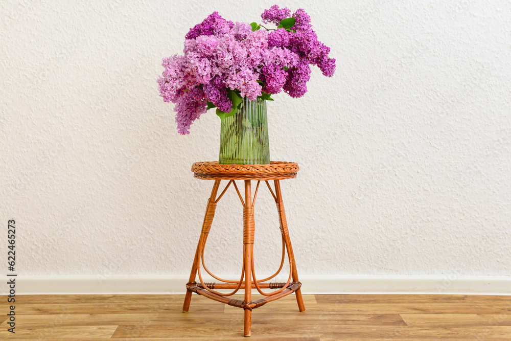 Vase with beautiful lilac flowers on table near light wall in room