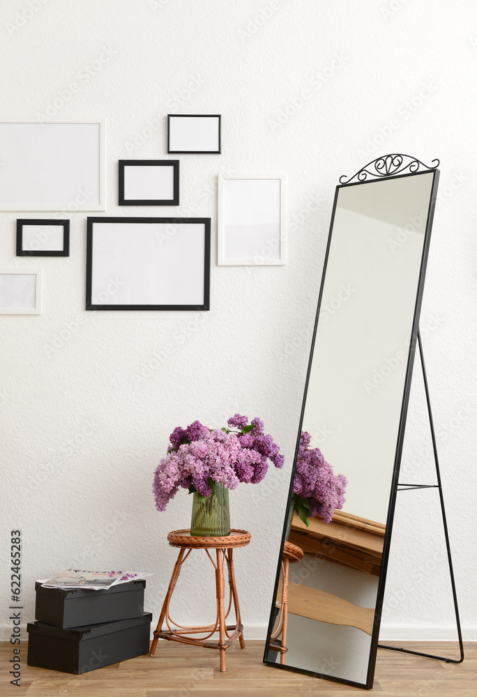 Vase with beautiful lilac flowers on table, mirror and blank pictures in interior of light living ro