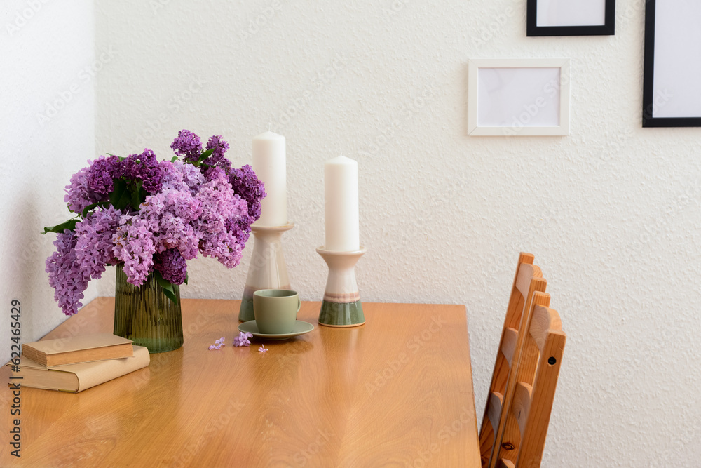 Vase with beautiful lilac flowers, candles on table and blank pictures in interior of light living r