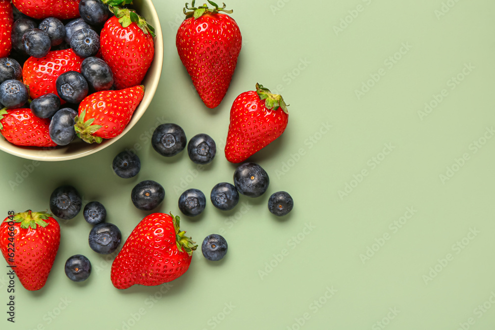 Bowl with fresh blueberries and strawberries on green background