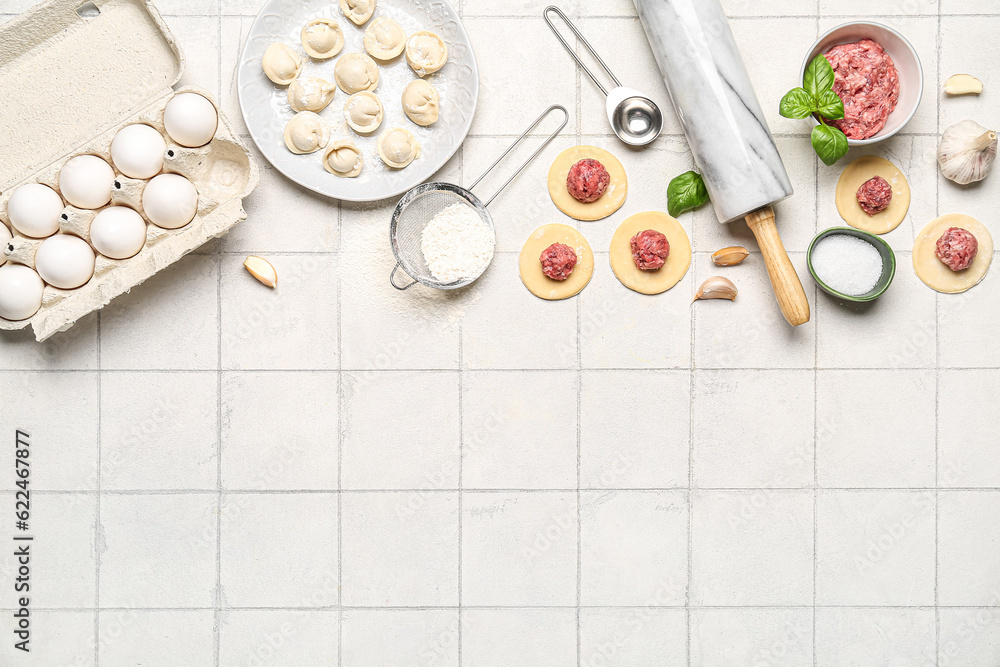 Plate with uncooked dumplings and ingredients on white tile background