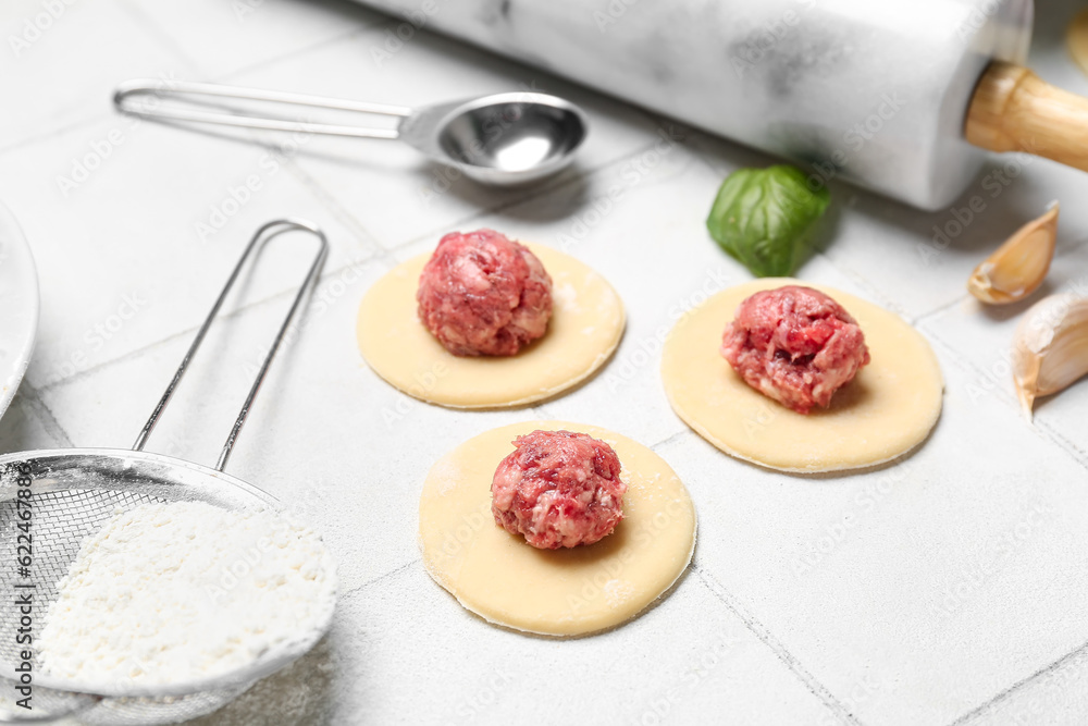 Raw dough with minced meat for preparing dumplings on white tile background