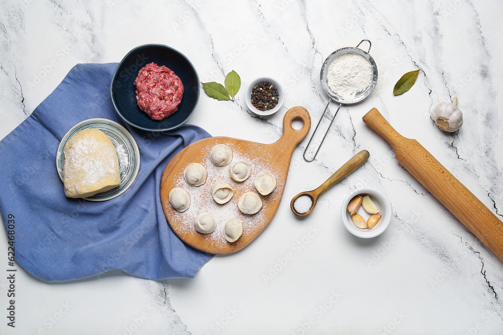 Wooden board with uncooked dumplings and ingredients on white marble background