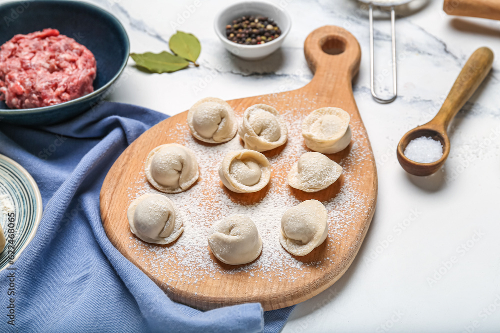 Wooden board with uncooked dumplings on white marble background