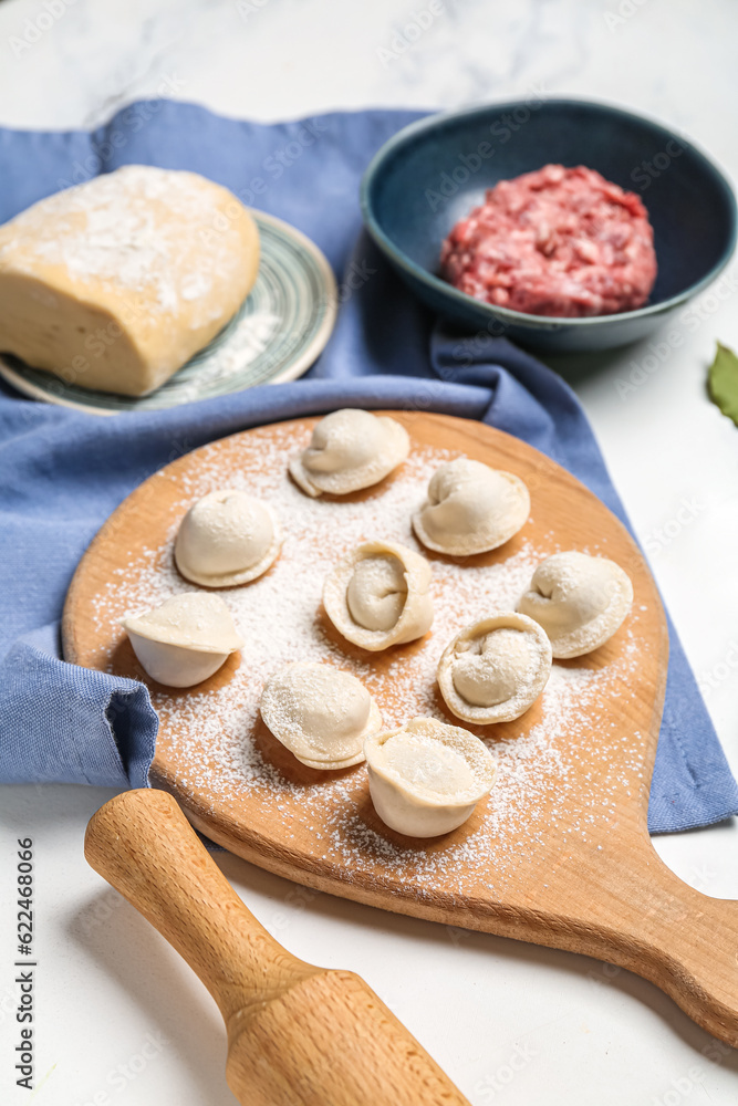 Wooden board with uncooked dumplings on light background