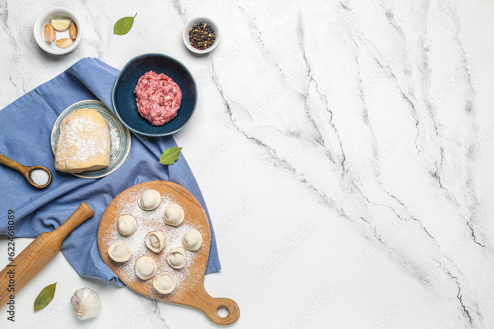 Wooden board with uncooked dumplings and ingredients on white marble background