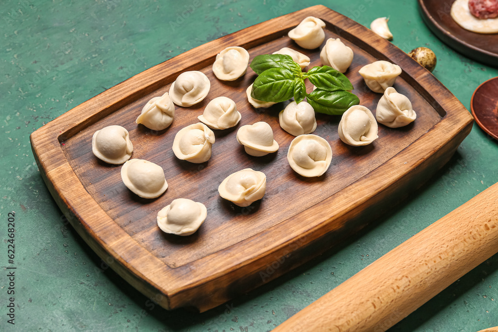 Wooden board with uncooked dumplings on green background