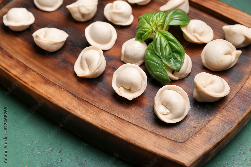 Wooden board with uncooked dumplings on green background